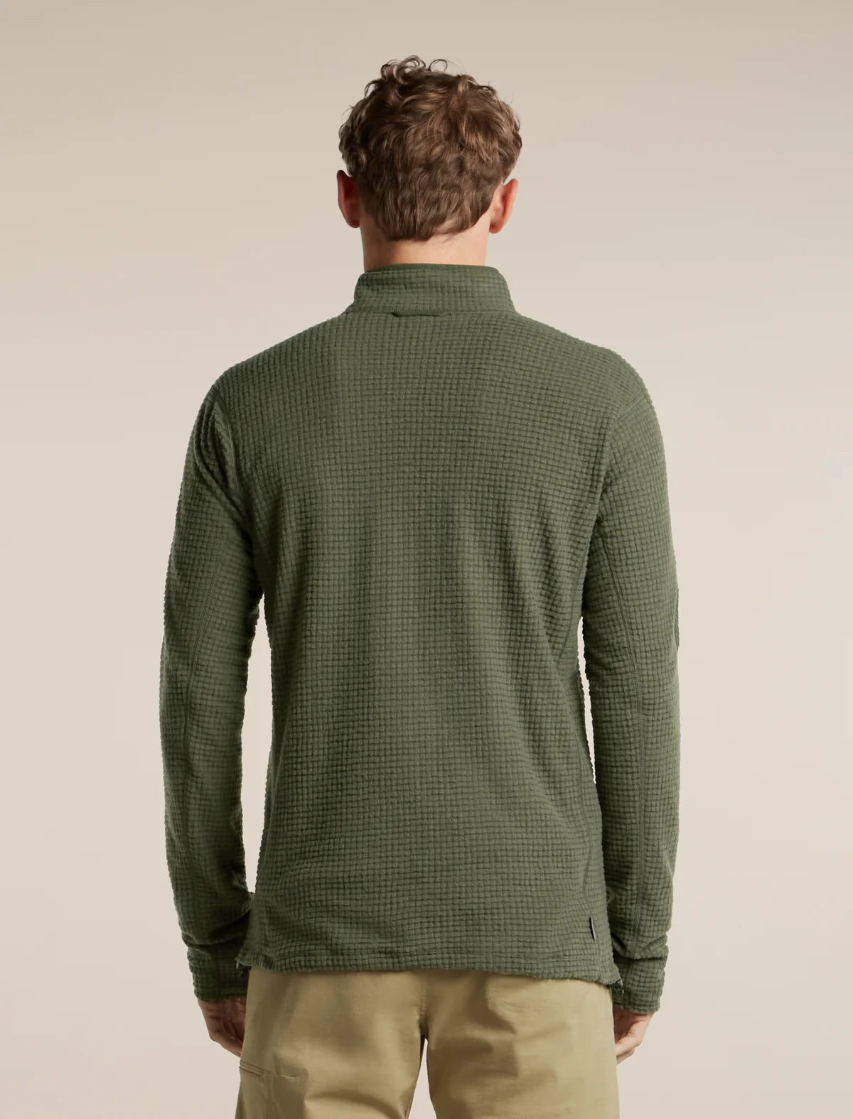 A man viewed from the back wearing an olive green waffle-knit quarter-zip pullover and khaki pants, set against a plain beige studio background. - Icebreaker Merino 400 RealFleece Grid Peaksland Long Sleeve Half Zip (Men's) - Dark Loden