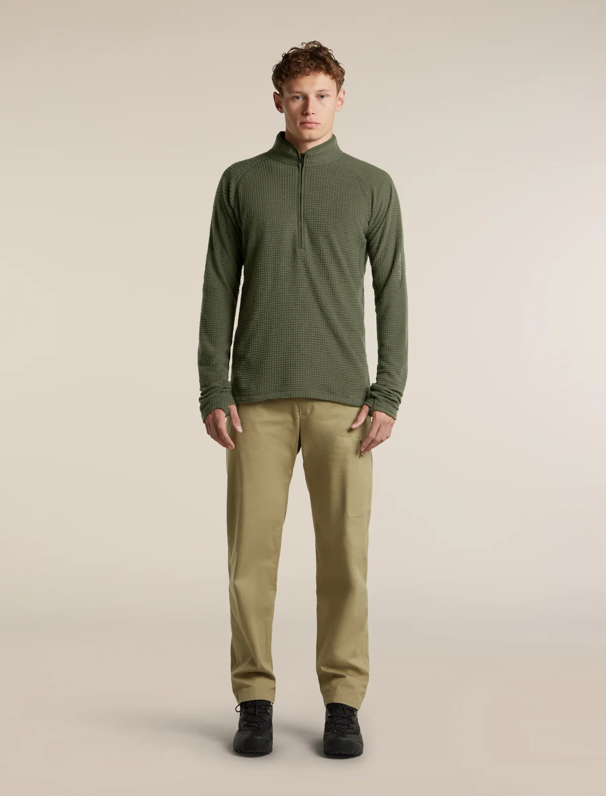 A man modeling a dark olive green quarter-zip long-sleeve shirt paired with khaki pants and black shoes, standing against a solid light beige studio background. - Icebreaker Merino 400 RealFleece Grid Peaksland Long Sleeve Half Zip (Men's) - Dark Loden