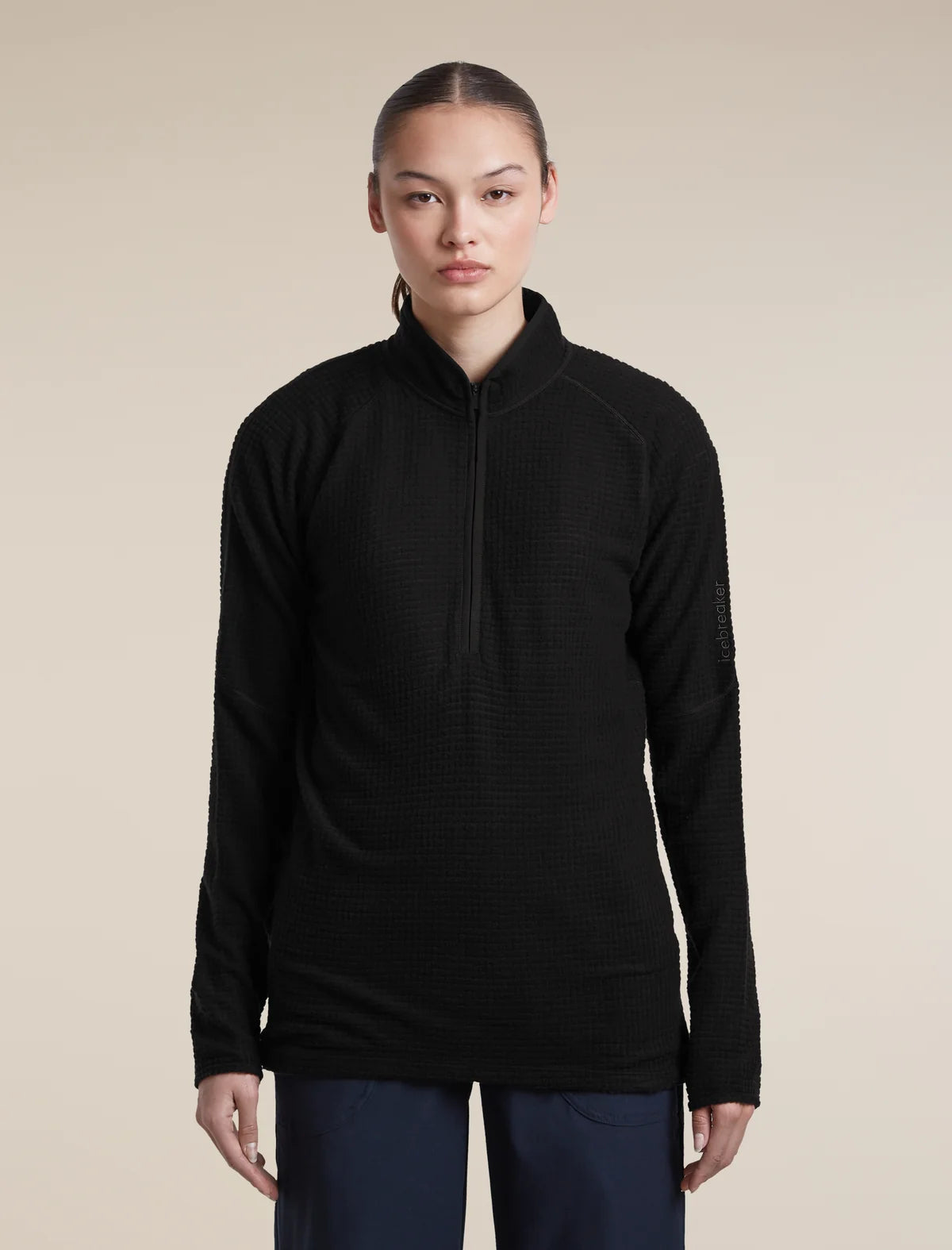 A woman modeling a black long-sleeve quarter-zip athletic pullover against a solid beige studio background. - Icebreaker Merino 400 RealFleece Grid Peaksland Long Sleeve Half Zip (Women's) - Black
