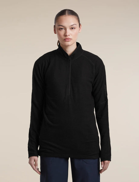 A woman modeling a black long-sleeve quarter-zip athletic pullover against a solid beige studio background. - Icebreaker Merino 400 RealFleece Grid Peaksland Long Sleeve Half Zip (Women's) - Black