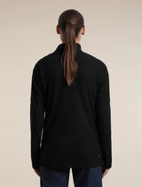 A woman viewed from the back wearing a black textured quarter-zip pullover sweater and dark trousers, set against a plain beige studio background. - Icebreaker Merino 400 RealFleece Grid Peaksland Long Sleeve Half Zip (Women's) - Black