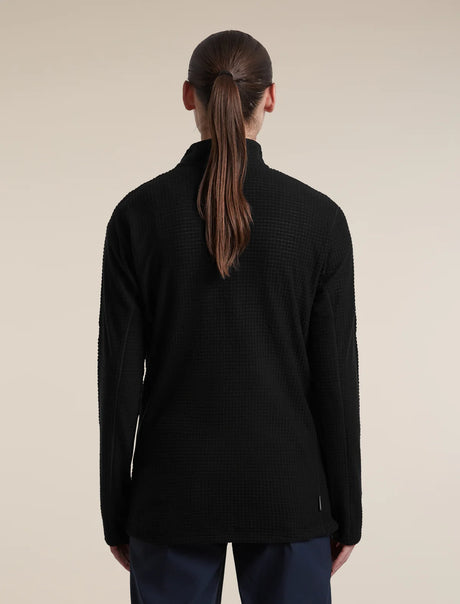 A woman viewed from the back wearing a black textured quarter-zip pullover sweater and dark trousers, set against a plain beige studio background. - Icebreaker Merino 400 RealFleece Grid Peaksland Long Sleeve Half Zip (Women's) - Black