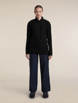 A model stands against a plain beige studio background wearing a black long-sleeve half-zip pullover, dark navy wide-leg trousers, and black shoes. - Icebreaker Merino 400 RealFleece Grid Peaksland Long Sleeve Half Zip (Women's) - Black