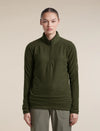 A model wearing an olive green waffle-knit quarter-zip pullover sweater and olive pants, standing against a solid beige background. - Icebreaker Merino 400 RealFleece Grid Peaksland Long Sleeve Half Zip (Women's) - Dark Loden
