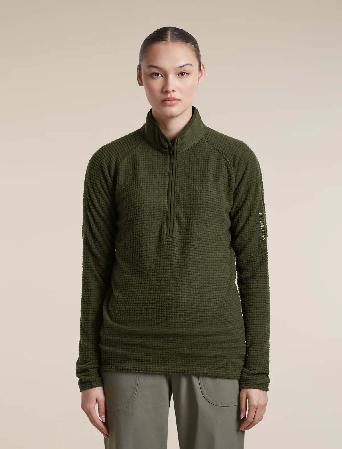 A model wearing an olive green waffle-knit quarter-zip pullover sweater and olive pants, standing against a solid beige background. - Icebreaker Merino 400 RealFleece Grid Peaksland Long Sleeve Half Zip (Women's) - Dark Loden
