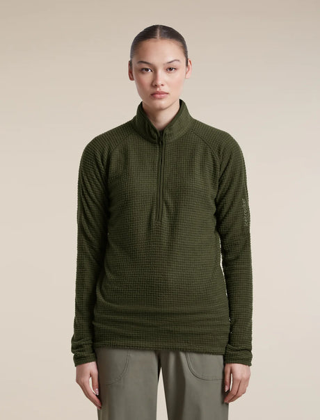 A model wearing an olive green waffle-knit quarter-zip pullover sweater and olive pants, standing against a solid beige background. - Icebreaker Merino 400 RealFleece Grid Peaksland Long Sleeve Half Zip (Women's) - Dark Loden