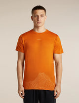 A man wearing a bright orange athletic t-shirt with a subtle white low-poly mountain graphic near the hem, standing against a neutral beige background. - Icebreaker Merino 150 Tech Lite Short Sleeve T-Shirt 3D Mapping (Men's) - Spice