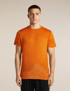 A man wearing a bright orange athletic t-shirt with a subtle white low-poly mountain graphic near the hem, standing against a neutral beige background. - Icebreaker Merino 150 Tech Lite Short Sleeve T-Shirt 3D Mapping (Men's) - Spice