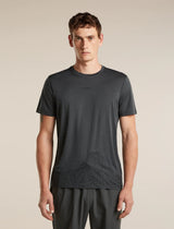 A man wearing a dark gray short-sleeve athletic t-shirt with a subtle mountain line-art graphic near the hem, paired with dark gray athletic pants, against a solid beige background. - Icebreaker Merino 150 Tech Lite Short Sleeve T-Shirt 3D Mapping (Men's) - Obsidian