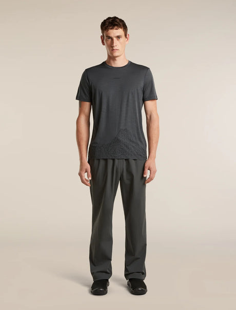 A man modeling a dark gray short-sleeve athletic t-shirt and matching dark gray pants against a solid light beige background. - Icebreaker Merino 150 Tech Lite Short Sleeve T-Shirt 3D Mapping (Men's) - Obsidian