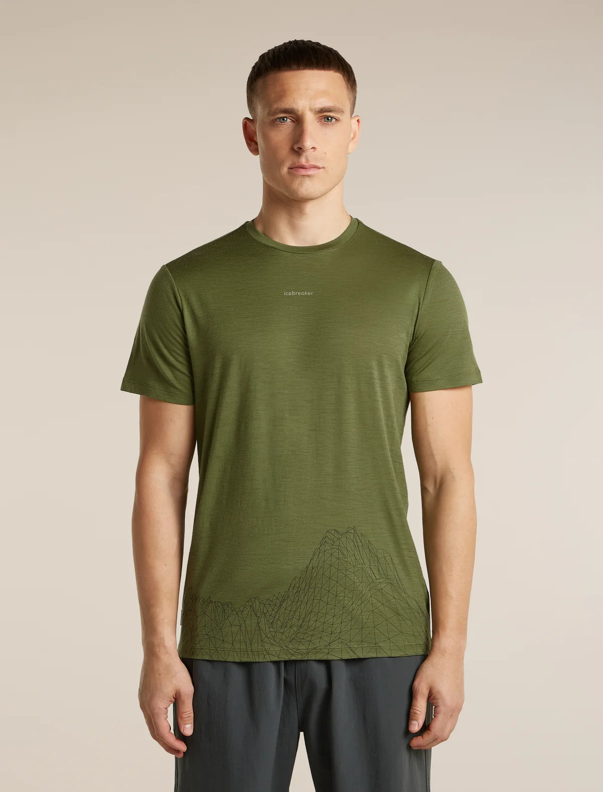 A man wearing an olive green athletic t-shirt with a subtle mountain line-art graphic near the hem, paired with dark gray athletic pants, standing against a solid beige background. - Icebreaker Merino 150 Tech Lite Short Sleeve T-Shirt 3D Mapping (Men's) - Sphagnum