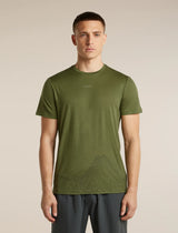 A man wearing an olive green athletic t-shirt with a subtle mountain line-art graphic near the hem, paired with dark gray athletic pants, standing against a solid beige background. - Icebreaker Merino 150 Tech Lite Short Sleeve T-Shirt 3D Mapping (Men's) - Sphagnum