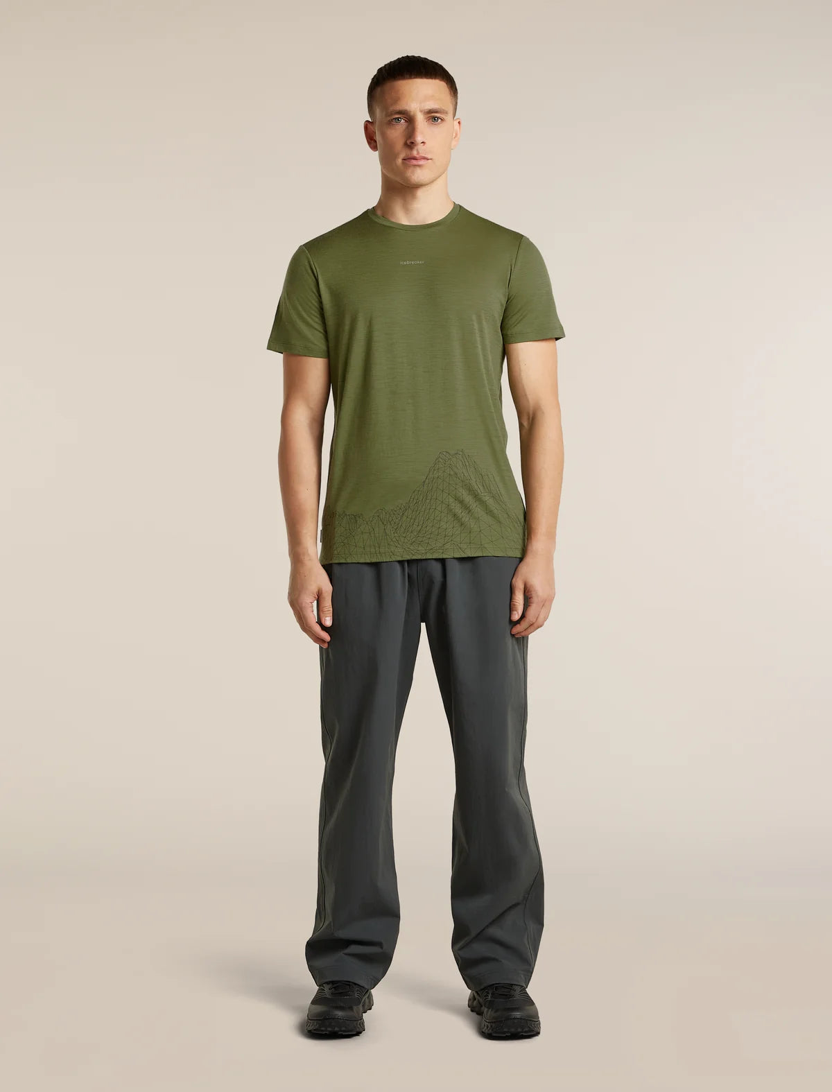 A man modeling an olive green short-sleeve athletic t-shirt with a subtle tonal graphic design on the lower front, paired with dark gray pants and black shoes, against a solid light beige background. - Icebreaker Merino 150 Tech Lite Short Sleeve T-Shirt 3D Mapping (Men's) - Sphagnum