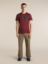 A man modeling a short-sleeve crewneck t-shirt in maroon with a dark graphic print across the chest, paired with khaki trousers and dark loafers, against a solid light beige background. - Icebreaker Merino 150 Tech Lite Short Sleeve T-Shirt Getaway (Men's) - Port