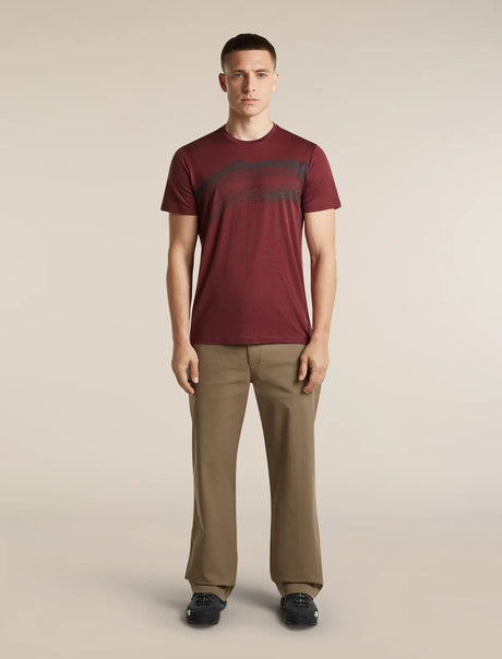 A man modeling a short-sleeve crewneck t-shirt in maroon with a dark graphic print across the chest, paired with khaki trousers and dark loafers, against a solid light beige background. - Icebreaker Merino 150 Tech Lite Short Sleeve T-Shirt Getaway (Men's) - Port
