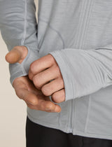 Close-up of a person wearing a gray athletic jacket with a beige background - Icebreaker 150 MerinoFine Ace Long Sleeve Zip Hoodie (Men's) - Proto Grey