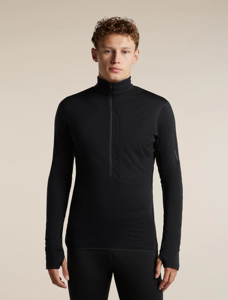 A man wearing a black long-sleeve half-zip athletic base layer top, paired with black leggings, standing against a solid beige studio background. - Icebreaker Merino Blend 200 RealFleece Descender Long Sleeve Half Zip (Men's) - Black