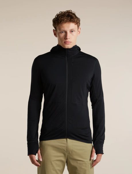 A man wearing a black long-sleeve athletic zip-up hoodie with a high collar, paired with khaki pants, standing against a solid beige studio background. - Icebreaker Merino Blend 200 RealFleece Descender Long Sleeve Zip Hoodie (Men's) - Black