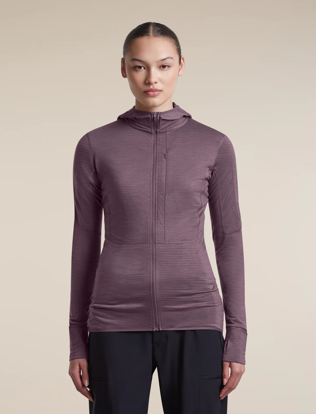 A woman modeling a long-sleeve, full-zip hooded athletic top in a muted plum-purple color, paired with dark pants, against a solid beige studio background. - Icebreaker Merino Blend 200 RealFleece Descender Long Sleeve Zip Hoodie (Women's) - Grey Plum - Purple