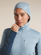 A close-up of a model wearing a light blue hooded zip-up jacket, holding the hood up. The background is a solid, warm off-white studio backdrop. - Icebreaker Merino Blend 300 RealFleece Descender Long Sleeve Zip Hoodie (Women's) - blue, light blue, dawn/zinc blue