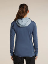 A woman shown from the back wearing a blue long-sleeve athletic hooded top and gray pants against a plain light beige studio background. - Icebreaker Merino Blend 300 RealFleece Descender Long Sleeve Zip Hoodie (Women's) - blue, light blue, dawn/zinc blue