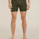 A man modeling dark olive green men's boxer briefs with a matching elastic waistband featuring the 'icebreaker' brand name, shown against a solid light beige background. - Icebreaker Merino 150 Anatomica Boxers (Men's) - Dark Loden
