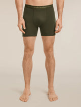 A man modeling dark olive green men's boxer briefs with a matching elastic waistband featuring the 'icebreaker' brand name, shown against a solid light beige background. - Icebreaker Merino 150 Anatomica Boxers (Men's) - Dark Loden