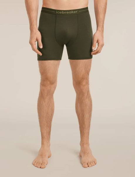 A man modeling dark olive green men's boxer briefs with a matching elastic waistband featuring the 'icebreaker' brand name, shown against a solid light beige background. - Icebreaker Merino 150 Anatomica Boxers (Men's) - Dark Loden