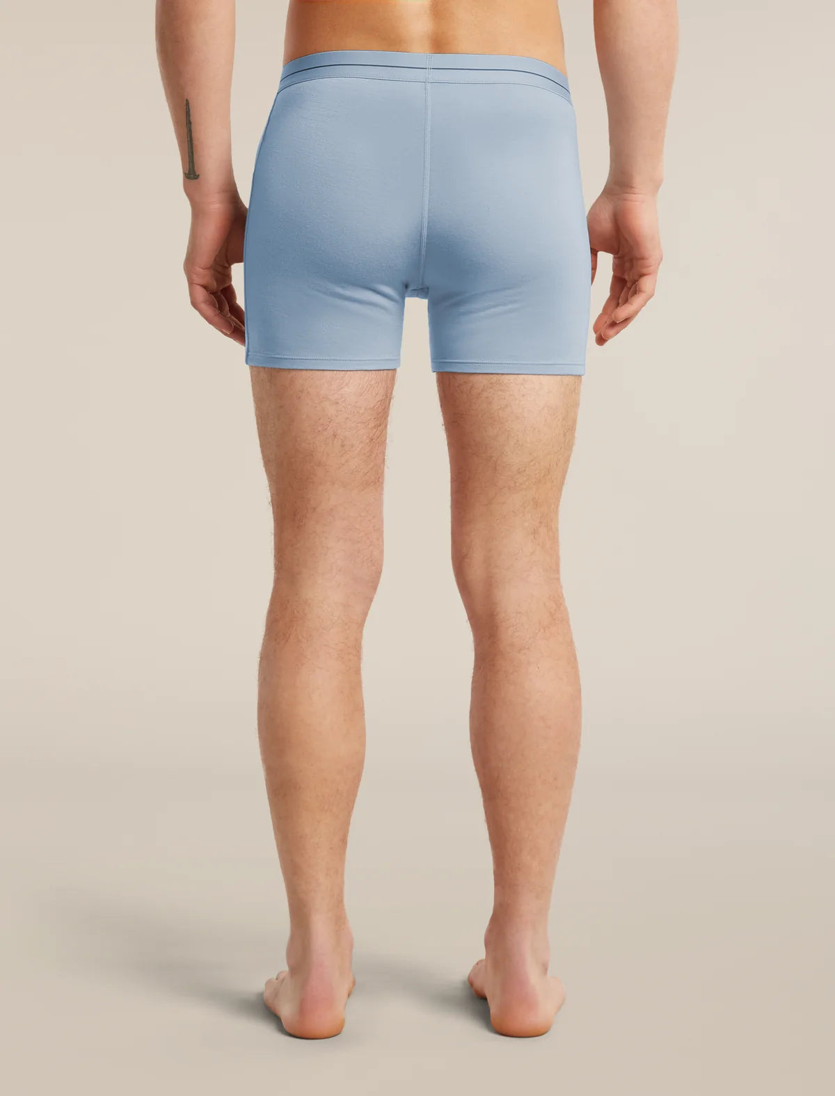 Rear view of a model wearing light blue athletic compression shorts against a warm beige studio background. - Icebreaker Merino 150 Anatomica Boxers (Men's) - Zinc Blue