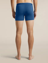 A man viewed from the back wearing blue boxer briefs, standing barefoot against a plain beige studio background. - Icebreaker Merino 150 Anatomica Boxers (Men's) - Lazurite