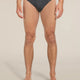 A man wearing dark gray heathered briefs with a black waistband featuring the white 'icebreaker' logo, shown from the waist down against a light beige studio background. - Icebreaker Merino 150 Anatomica Briefs (Men's) - Jet Heather