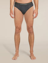A man wearing dark gray heathered briefs with a black waistband featuring the white 'icebreaker' logo, shown from the waist down against a light beige studio background. - Icebreaker Merino 150 Anatomica Briefs (Men's) - Jet Heather