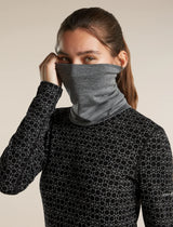 A woman wearing a dark gray heathered neck gaiter mask and a black long-sleeve athletic top with a white geometric honeycomb pattern, set against a solid beige background. - Icebreaker Merino 260 Apex Chute (Unisex) - Gritstone Heather