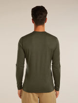 A man viewed from behind wearing an olive green long-sleeve crewneck shirt and khaki pants, standing against a plain light beige studio background. - Icebreaker Merino 200 Oasis Long Sleeve Crew Thermal Top (Men's) - Dark Loden