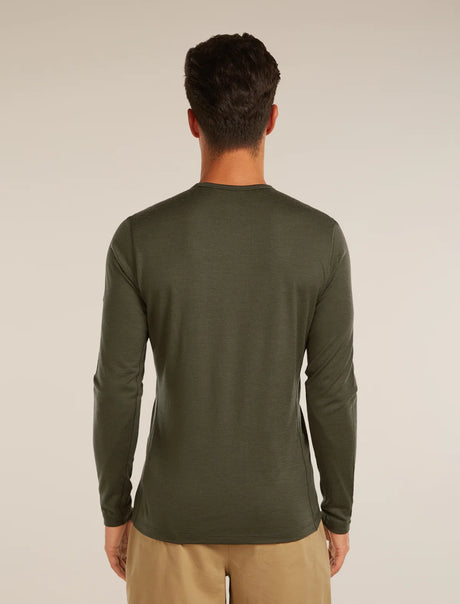 A man viewed from behind wearing an olive green long-sleeve crewneck shirt and khaki pants, standing against a plain light beige studio background. - Icebreaker Merino 200 Oasis Long Sleeve Crew Thermal Top (Men's) - Dark Loden