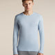 A man wearing a light blue long-sleeve crewneck athletic shirt and gray leggings, standing against a solid beige studio background. - Icebreaker Merino 200 Oasis Long Sleeve Crew Thermal Top (Men's) - Zinc Blue
