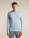 A man wearing a light blue long-sleeve crewneck athletic shirt and gray leggings, standing against a solid beige studio background. - Icebreaker Merino 200 Oasis Long Sleeve Crew Thermal Top (Men's) - Zinc Blue