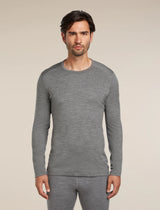 A man wearing a heather gray long-sleeve crewneck shirt and matching gray pants, standing against a plain beige studio background. - Icebreaker Merino 260 Oasis Long Sleeve Crew Thermal Top (Men's) - Gritstone Heather