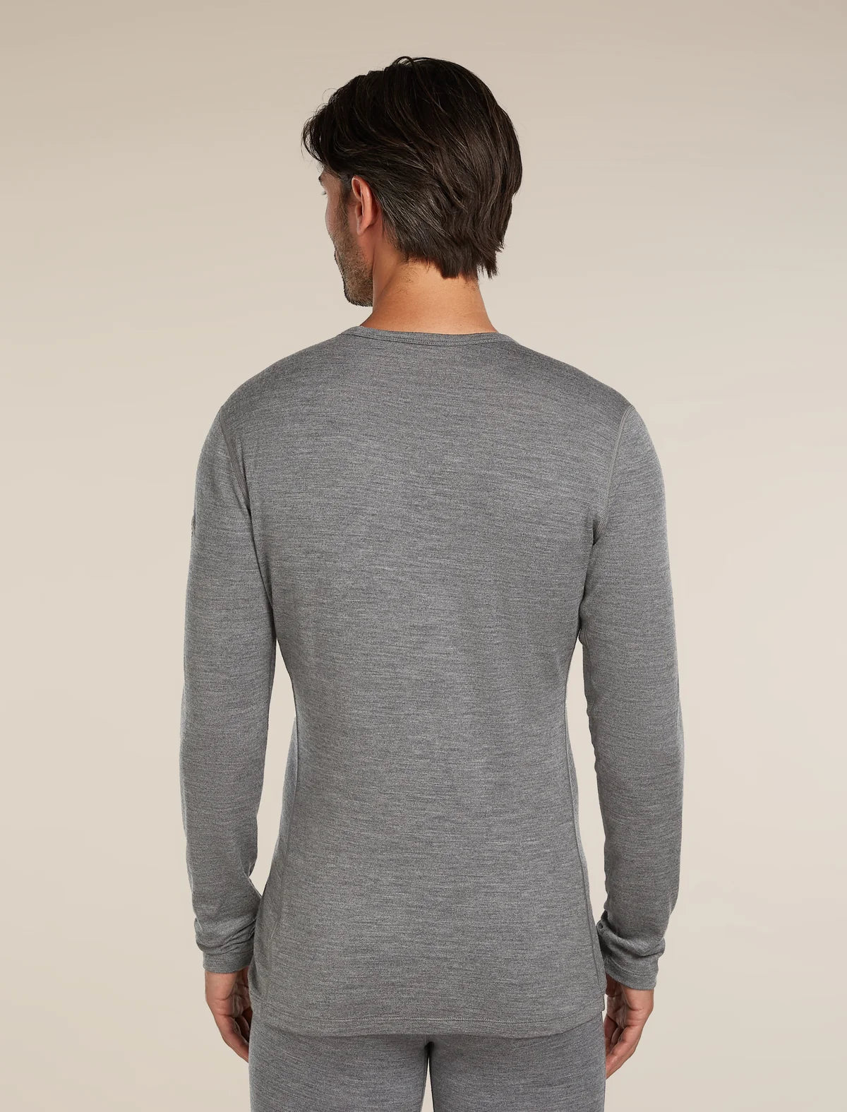 A man viewed from the back wearing a heather gray long-sleeve crewneck shirt and matching gray pants against a plain beige studio background. - Icebreaker Merino 260 Oasis Long Sleeve Crew Thermal Top (Men's) - Gritstone Heather
