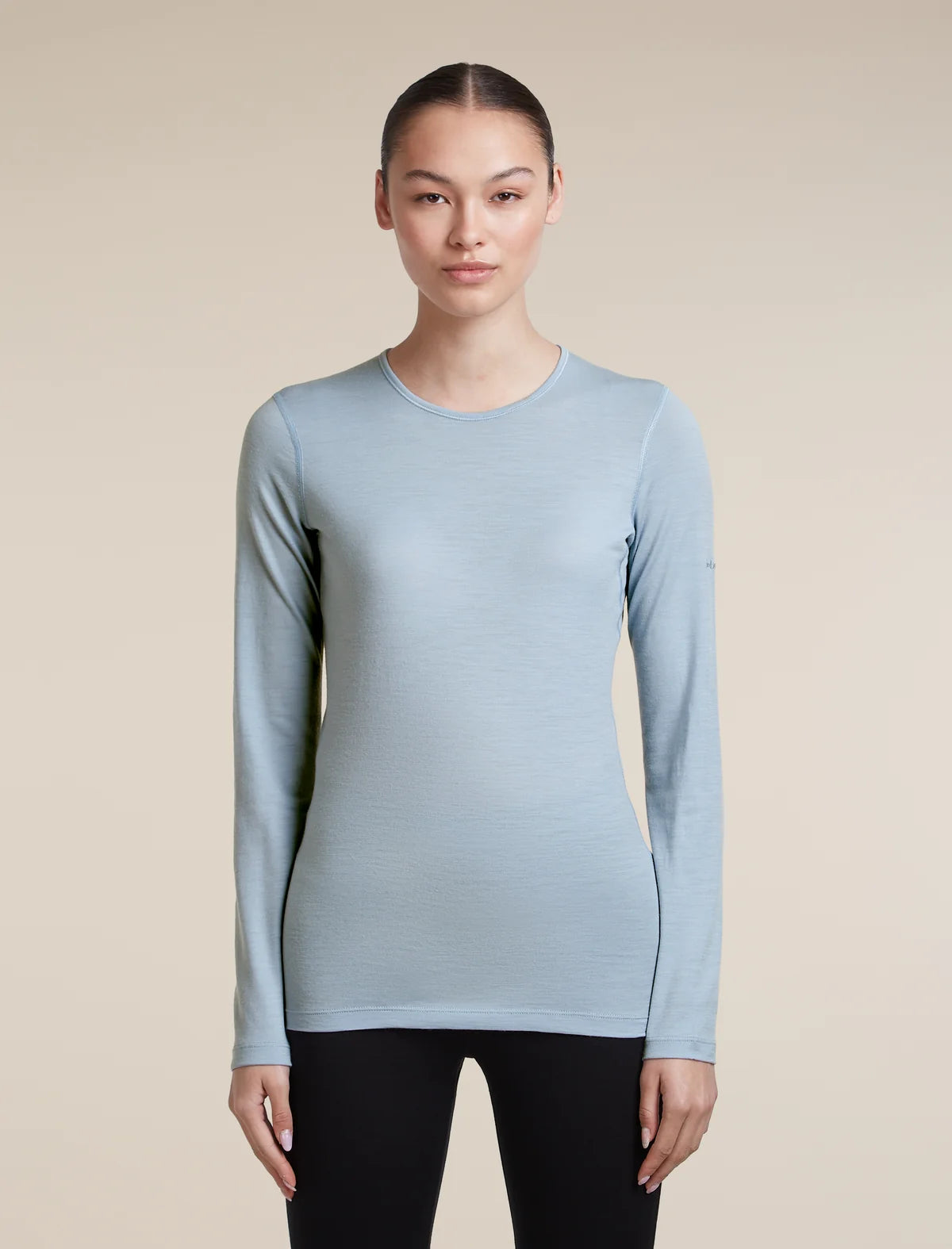 A woman modeling a light blue long-sleeve crewneck athletic top against a solid beige background. - Icebreaker Merino 200 Oasis Long Sleeve Crew Thermal Top (Women's) - Zinc Blue