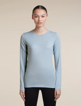 A woman modeling a light blue long-sleeve crewneck athletic top against a solid beige background. - Icebreaker Merino 200 Oasis Long Sleeve Crew Thermal Top (Women's) - Zinc Blue