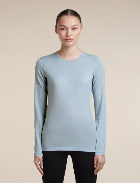 A woman modeling a light blue long-sleeve crewneck athletic top against a solid beige background. - Icebreaker Merino 200 Oasis Long Sleeve Crew Thermal Top (Women's) - Zinc Blue
