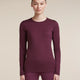 A woman modeling a long-sleeve crewneck top and matching leggings in a deep plum purple color, set against a solid beige studio background. - Icebreaker Merino 200 Oasis Long Sleeve Crew Thermal Top (Women's) - Dark Berry