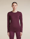 A woman modeling a long-sleeve crewneck top and matching leggings in a deep plum purple color, set against a solid beige studio background. - Icebreaker Merino 200 Oasis Long Sleeve Crew Thermal Top (Women's) - Dark Berry