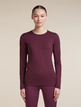 A woman modeling a long-sleeve crewneck top and matching leggings in a deep plum purple color, set against a solid beige studio background. - Icebreaker Merino 200 Oasis Long Sleeve Crew Thermal Top (Women's) - Dark Berry