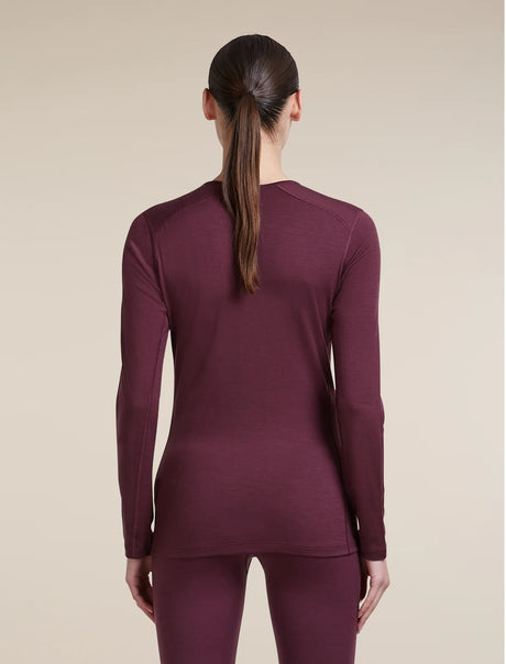 A woman viewed from the back wearing a fitted long-sleeve crew-neck top and matching leggings in a deep plum-burgundy color, against a plain warm beige studio background. - Icebreaker Merino 200 Oasis Long Sleeve Crew Thermal Top (Women's) - Dark Berry