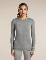 A woman modeling a fitted long-sleeve crewneck top in heather gray, paired with matching gray leggings, against a plain beige studio background. - Icebreaker Merino 260 Oasis Long Sleeve Crew Thermal Top (Women's) - Metro Heather