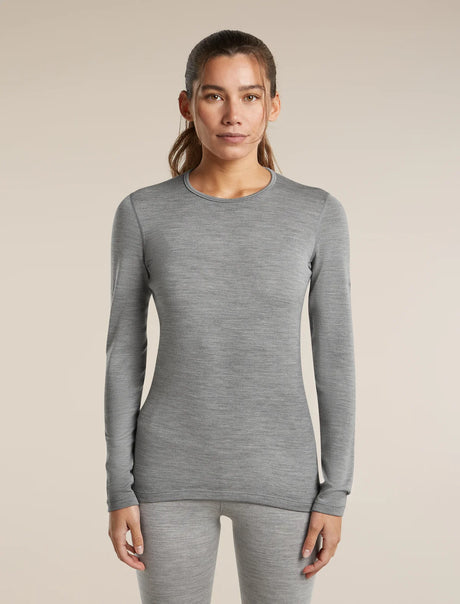 A woman modeling a fitted long-sleeve crewneck top in heather gray, paired with matching gray leggings, against a plain beige studio background. - Icebreaker Merino 260 Oasis Long Sleeve Crew Thermal Top (Women's) - Metro Heather