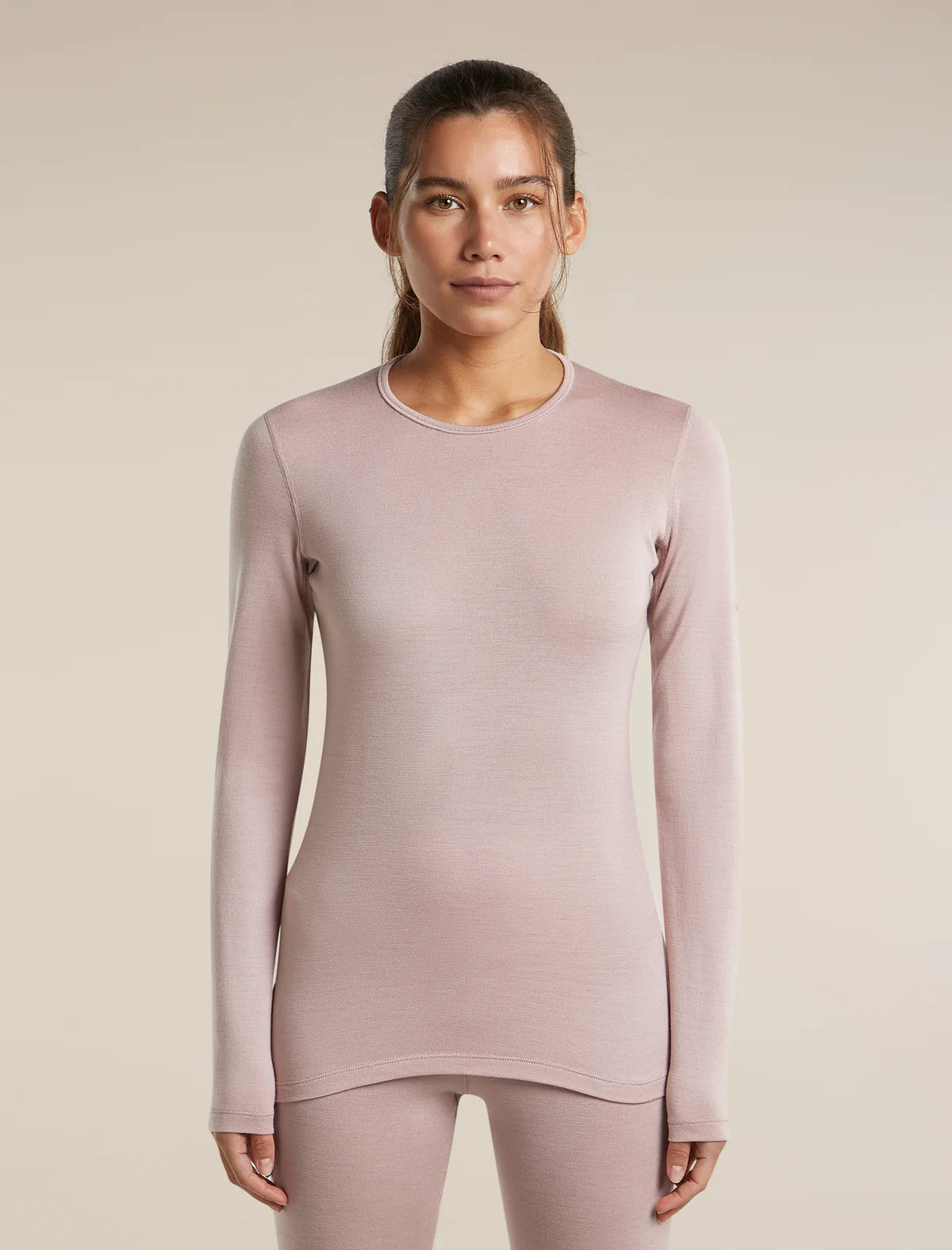 A woman modeling a long-sleeve crewneck top in a dusty mauve-pink color, paired with matching leggings, against a solid light beige background. - Icebreaker Merino 260 Oasis Long Sleeve Crew Thermal Top (Women's) - Pink Quartz
