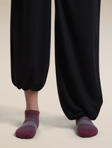 A close-up of a person's feet wearing dark charcoal black harem-style pants and burgundy low-cut socks with gray striped detailing, set against a solid light beige background. - Icebreaker Merino Multisport Light Micro Socks (Women's) - Dark Berry/Midnight Navy/Grey Plum